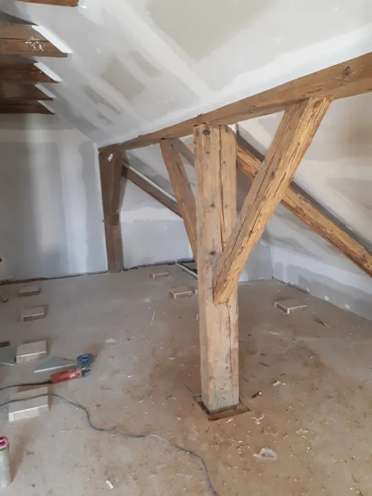 Sichtbare Holzstützen unter einer teilweise verspachtelten Dachschräge