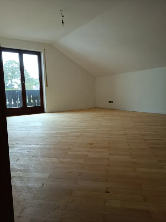Renovierter Dachgeschossraum mit weißen Wänden, Dachschräge und Parkett