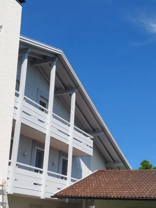 Weiße Hausfassade mit Holzbalkonen vor blauem Himmel