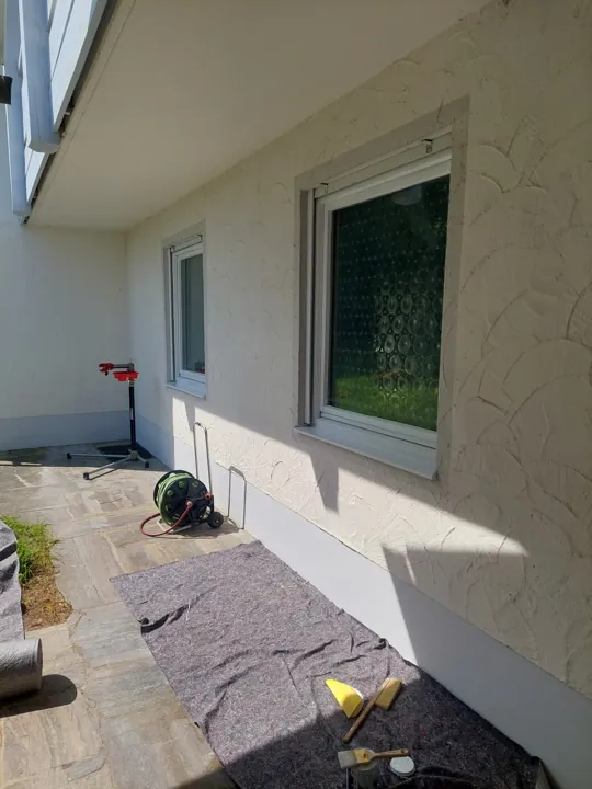 Helle verputzte Fassade mit weißen Fenstern und geschütztem Boden