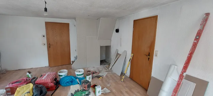 Wohnraum während der Renovierung mit weißer Kaminverkleidung, Werkzeug und abgedecktem Boden